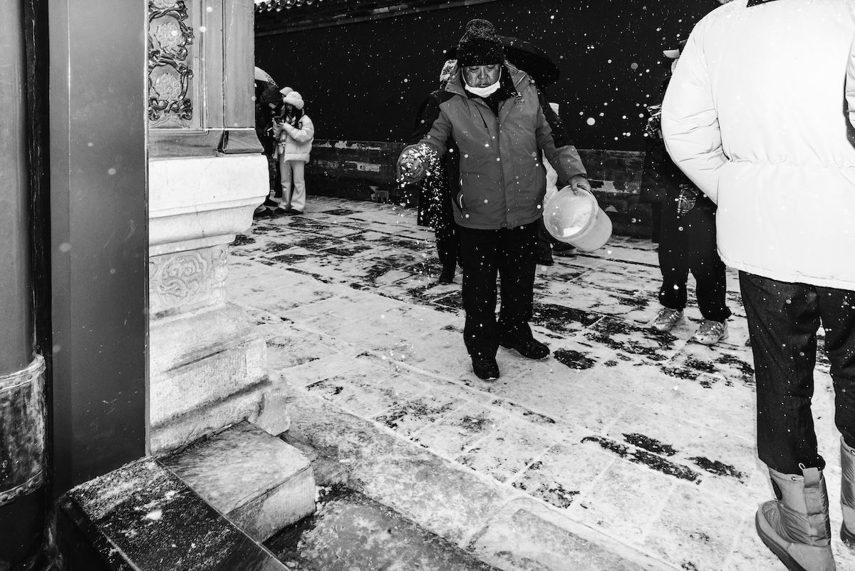 戴白口罩的冬装老人在扫石阶上的雪。